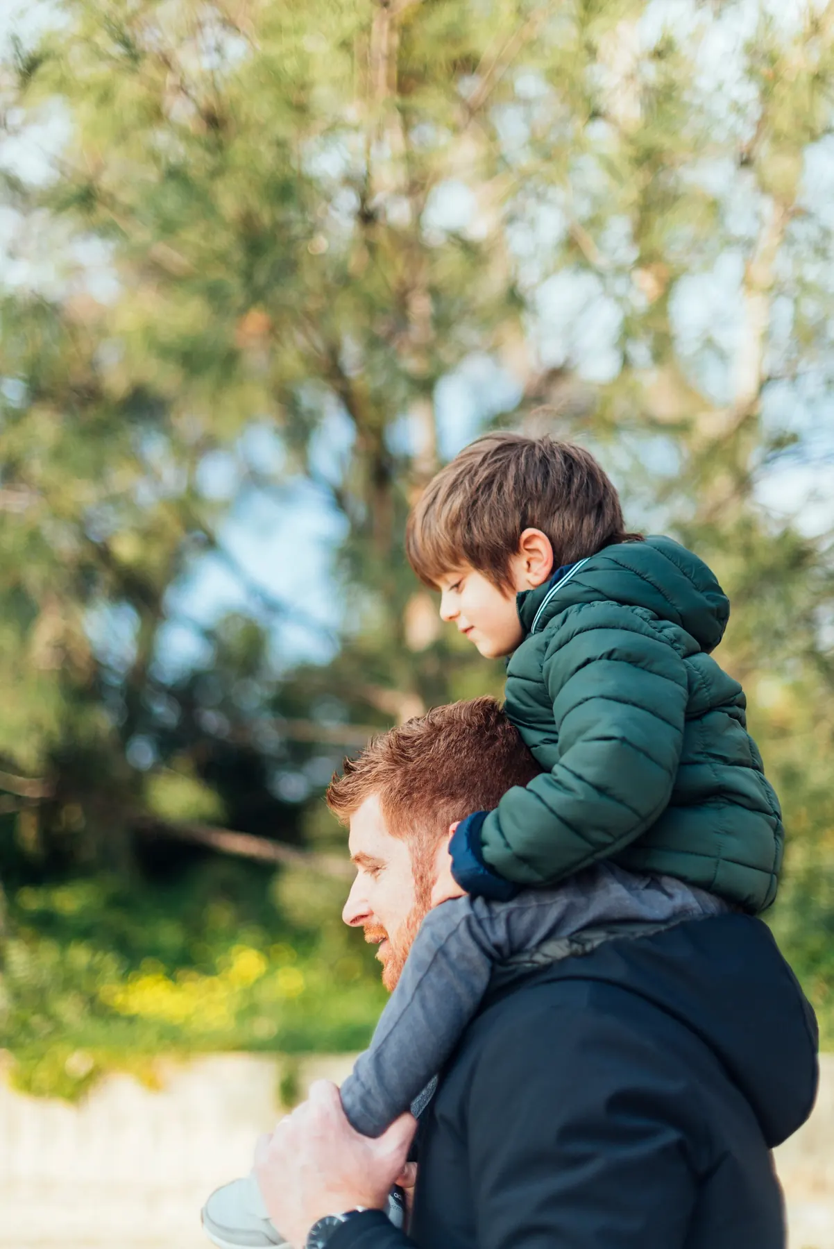 A young boy riding on a man’s shoulders on a walk outdoors