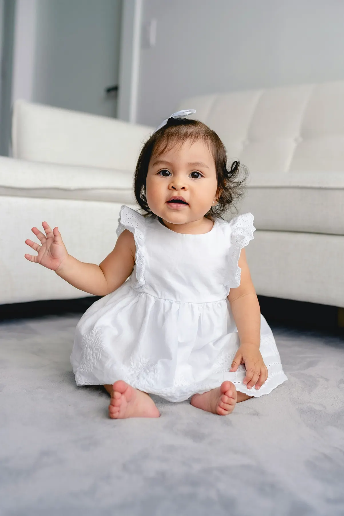 A baby girl in a white dress waving