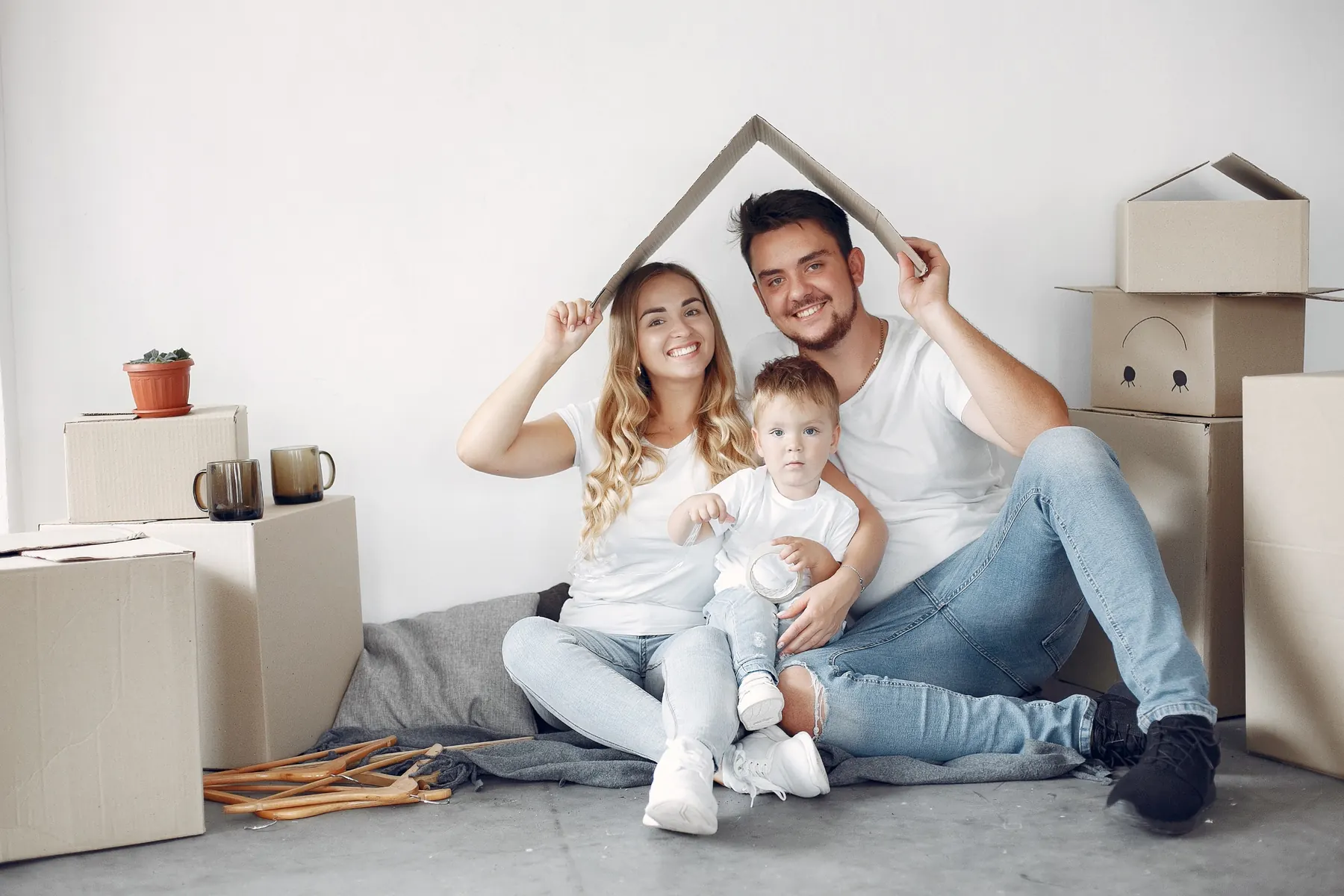A couple and their toddler under a cardboard roof among moving boxes