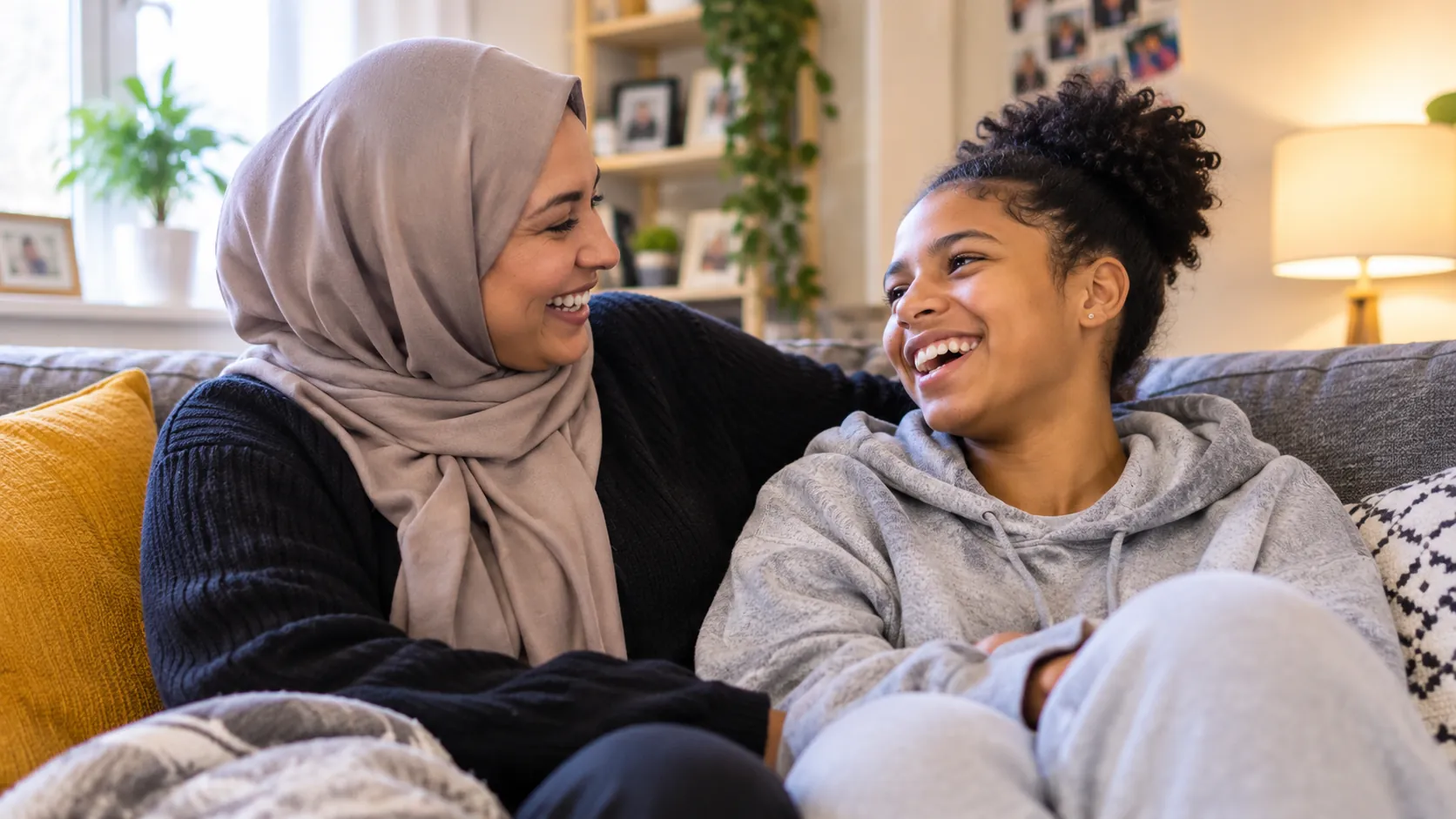 A foster carer and a teenage girl laughing together on the sofa at home