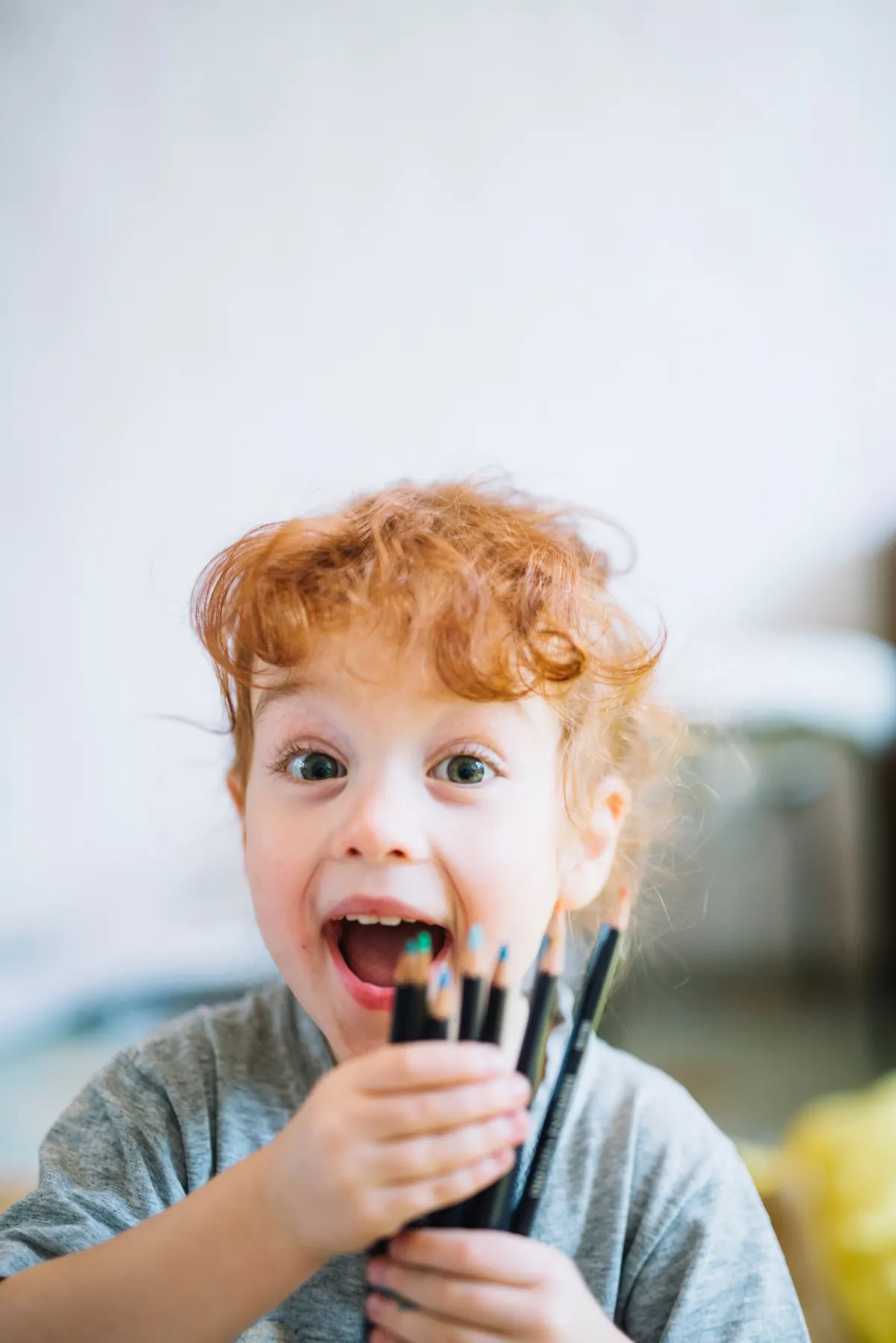 A delighted young child holding a handful of colouring pencils